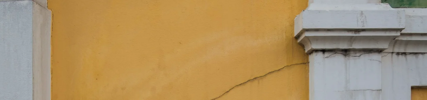 An exterior yellow wall with cracks on it