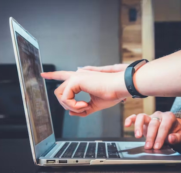 A laptop is lying open with something on it's screen and a hand are pointing towards the screen.