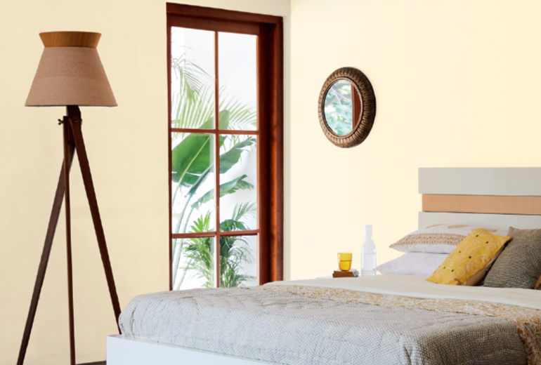 A bedroom painted with Pale Sisal Shade walls, a bed by a wooden window with a lampshade and mirror on the wall