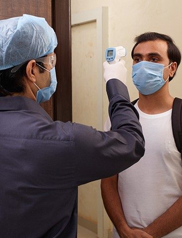 A supervisor in safety gear and mask checking the temperature of a trained applicator wearing mask.