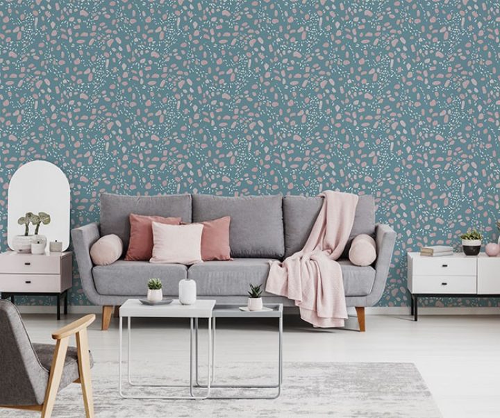 Pink blanket and cushions on grey settee in white flat interior with poster above cupboard. Real photo